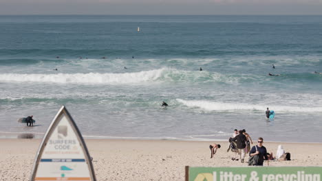 Kleine-Wellen-Rollen-In-Den-Bondi-Beach-Und-Schilder-Zeigen-Den-Surfer-Code-Und-Helfen-Dabei,-Den-Strand-Sauber-Zu-Machen