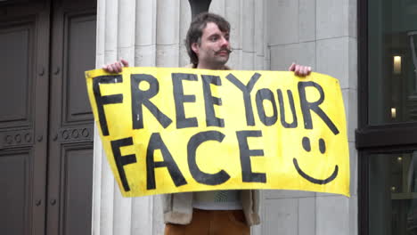 A-protestors-holds-up-a-yellow-placard-that-says,-“Free-your-face”-on-a-Coronavirus-and-QAnon-conspiracy-protest-opposing-compulsory-face-masks-and-anti-lockdown-measures