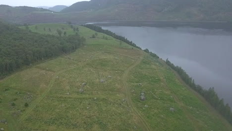 Aerial-View-Of-a-grassy-field-along-side-a-Lake-in-Hjelmeland,-Norway
