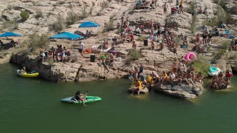 People-gather-on-rocky-riverbank-on-lazy,-hot,-sunny-summer-day