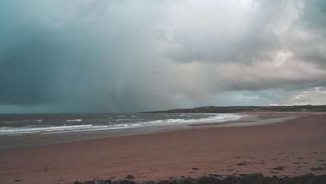 Grey-stormy-rain-clouds-over-an-empty-beach-with-waves-crashing-in-South-Shields,-UK