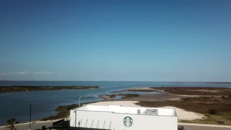 Aerial-reveal-of-Starbucks-Cafe-and-parking-lot-on-Laguna-Madre-with-small-natural-islands-in-the-background