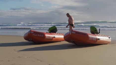 Hombre-Caminando-En-La-Playa-Hacia-El-Océano---Dos-Botes-De-Goma-Inflables-En-La-Playa-De-Currumbin---Costa-Dorada,-Queensland,-Australia