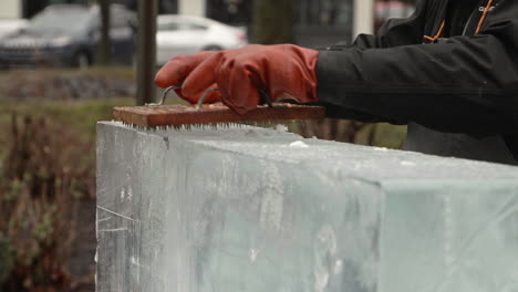 Shavings-flying-off-of-ice-block-as-sculptor-uses-nail-board,-Front-Angle,-Slow-Motion