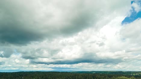 Stunning-cumulus-nimbus-clouds-roll-across-a-densely-forested-landscape,-aerial-hperlapse