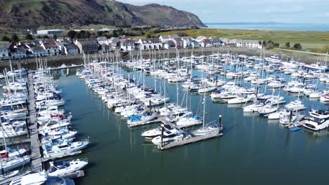 Luxury-yachts-and-sailboats-moored-in-Conwy-marina-mountain-waterfront-aerial-view-North-Wales-rise-tilt-down