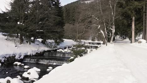 Wide-shot-showing-small-flowing-waterfall-in-nature-during-snowy-winter-day-in-forest-landscape
