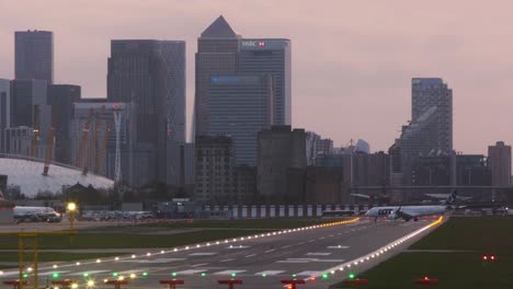 Kleines-Flugzeug,-Das-Auf-Der-Landebahn-Des-London-City-Airport-Abdreht,-Am-Abend-Canary-Wharf-Im-Hintergrund