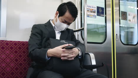 Japanischer-Männlicher-Pendler-Mit-Maske,-Der-Während-Einer-Pandemie-Im-Zug-Sitzt-Und-Schläft