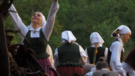 Adult-caucasian-dancers-in-traditional-folk-costumes-perform-in-a-dance-performance-in-open-air,-sunny-summer-evening,-happy,-Latvian-national-culture,-medium-shot-from-a-distance
