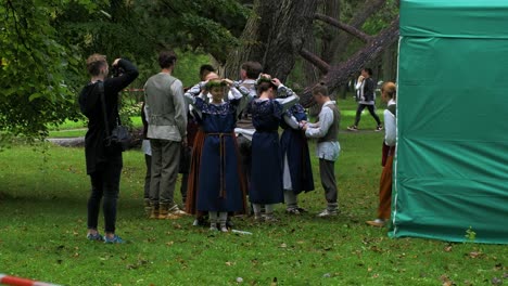 Group-of-adult-caucasian-dancers-in-traditional-folk-costumes-preparing-for-a-dance-performance-in-open-air,-sunny-summer-evening,-happy,-Latvian-national-culture,-medium-distant-shot