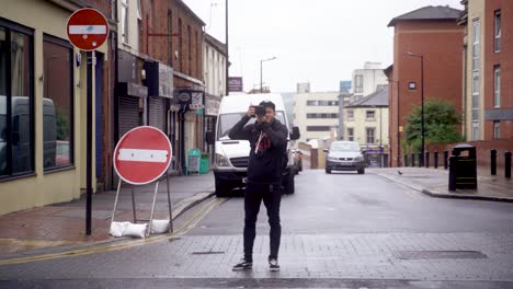 Handheld-static-shot-of-man-standing-on-other-side-of-street-with-camera-while-bus-and-cars-pass,-West-Street,-Sheffield,-England