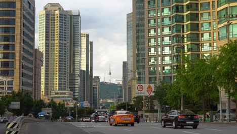 Der-Verkehr-Fährt-In-Der-Stadt-Vorbei-An-Hochhäusern-Mit-Dem-Namsan-Turm-Im-Hintergrund-In-Seoul,-Südkorea
