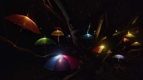 Farbenfrohe-Nächtliche-Lichtkunstausstellung-Von-Regenschirmen-Draußen-In-Bäumen-In-Heligan,-Cornwall-–-Schwenkaufnahme