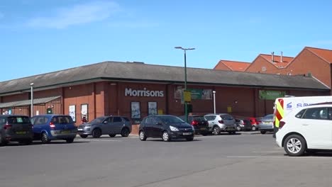 Cars-moving,-and-people-walking-in-and-out-of-a-modest-sized-supermarket-in-England