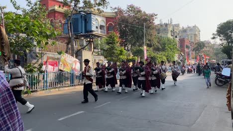 Vista-Estática-De-Una-Banda-Juvenil-Marchando-Y-Tocando-Instrumentos-Musicales-En-La-Carretera-Seguida-Por-La-Procesión-Del-Partido-Tmc-Para-Atraer-A-Los-Votantes-Antes-De-Las-Encuestas-Cívicas-De-Kolkata-En-Una-Tarde-De-Invierno