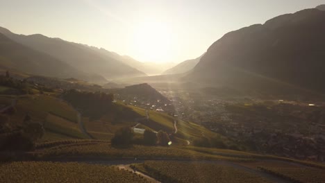 Drone-shot-in-the-early-morning-with-the-sun-rising-in-the-distance-over-a-beautiful-mountain-valley-in-Lavaux-Oron,-Switzerland-in-4k