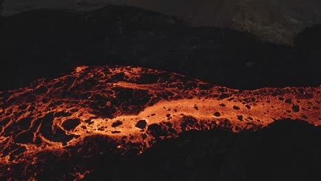 Drone-flying-over-golden-lava-running-through-black-rocks