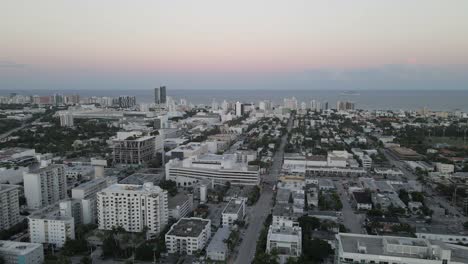 Dawn-aerial-POV-follows-street-in-South-Beach-Miami,-Atlantic-beyond