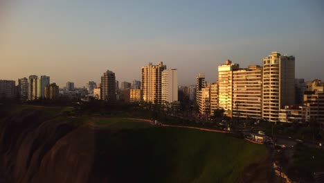 AERIAL---Sunrise-and-luxury-buildings,-Miraflores,-Lima,-Peru,-wide-shot-forward