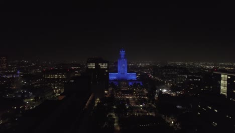 Nachtweite-Luftaufnahme-Des-Fluges-In-Richtung-Des-Rathauses-Von-Los-Angeles,-Beleuchtet-In-Blauem-Licht-Zu-Ehren-Des-Gesundheitswesens-Und-Wichtiger-Arbeitskräfte