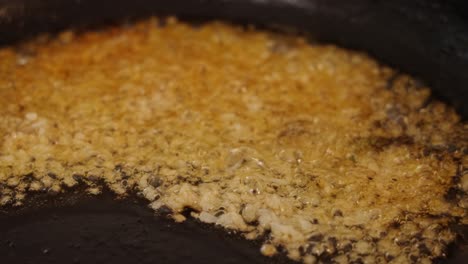 Close-up-shot-of-pan-frying,-sauteing-and-caramelizing-miced-garlic,-boiling-in-shimmering-cooking-oil-with-high-heat,-aromatic-smell-and-sizzling-sound