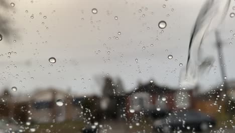 Regnerischer-Fensterhintergrund-Mit-Regentropfen,-Die-Auf-Der-Oberfläche-Fließen,-Mit-Städtischen-Häusern-Als-Verschwommenem-Hintergrund,-Traurige-Stimmung