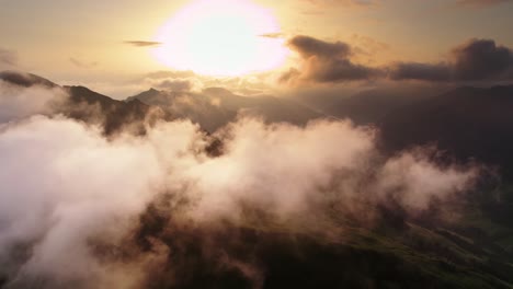 Droneshot-flying-above-and-through-the-clouds-releasing-the-view-on-mountainrange-and-valleys-in-Austria-with-sun-very-low