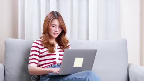 Junge-Asiatische-Frau,-Die-Auf-Sofa-Sitzt-Und-Notizbuch-Verwendet,-Um-Online-Einzukaufen