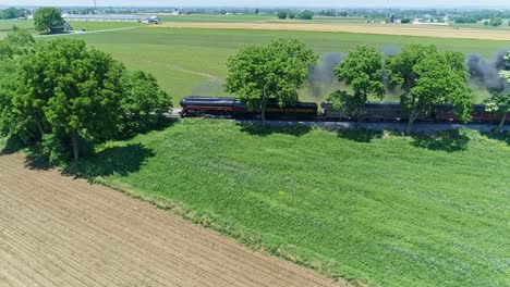 Aerial-View-of-an-Antique-Steam-Engine-and-Passenger-Coaches-Traveling-Along-Countryside-Blowing-Smoke-and-Drone-Traveling-Parallel-To-It,-on-a-Sunny-Summer-Day