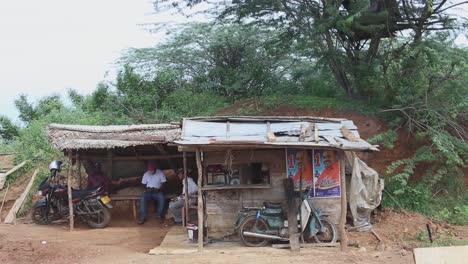 Vista-De-Gente-Asiática-Tomando-Una-Taza-De-Té-En-Un-Pobre-Puesto-De-Té-Al-Lado-De-La-Carretera-Y-Uno-De-Ellos-Se-Levanta-Después-De-Tomar-Una-Galleta-Para-Conseguir-Su-Taza-De-Té