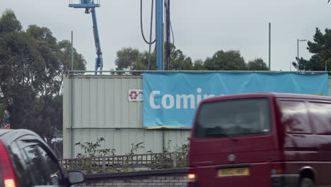 Banner-On-Steel-Fence-At-The-Construction-Site-Of-Aldi-Supermarket-In-Garras-Wharf,-Truro,-Cornwall-With-Daytime-Traffic-In-Foreground