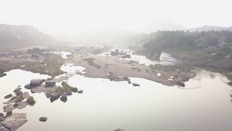 Surrealer-High-Key-Flussnebel-Mit-Felsbrocken-Und-Palmen-In-Hampi,-Indien