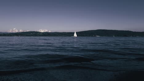 Cinematic-dark-colored-low-angle-view-of-yacht-cruise-in-calm-open-lake-waters-of-Maggiore-lake-in-Italy