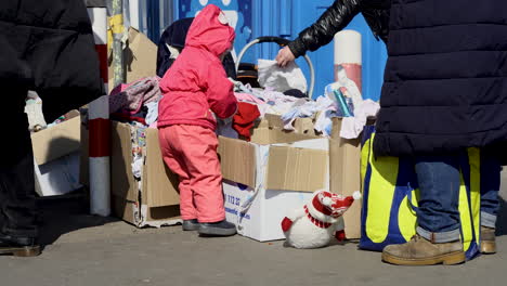 A-little-girl-in-red-clothes-looks-for-toys-in-a-tent-with-gifts-for-refugees-from-Ukraine
