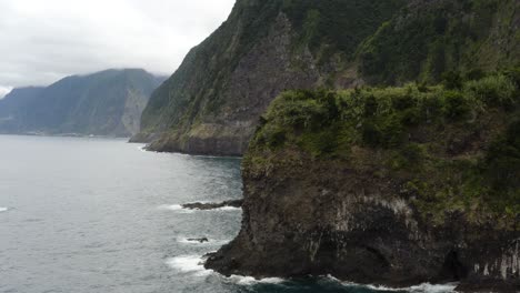 Aerial-is-flying-along-the-coast-of-Seixal-and-reveals-a-small-waterfall,-madeira