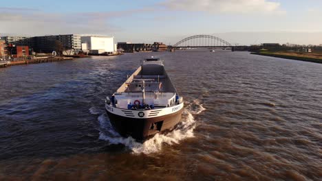 Aerial-View-Of-Forward-Bow-Of-Fenny-II-Inland-Container-Vessel-Along-River-Noord-With-Bridge-over-the-Noord-In-Background