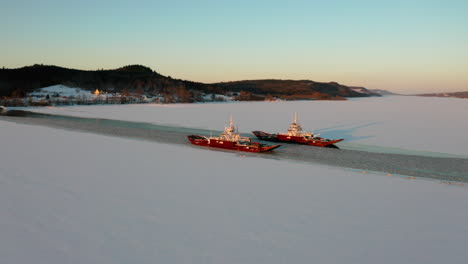 Luftaufnahme-Von-Zwei-Vorbeifahrenden-Autofähren,-Die-Bei-Sonnenuntergang-Einen-Schneebedeckten-Fluss-überqueren