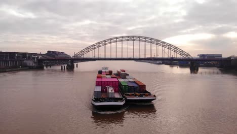 Aerial-Of-Excelsior-Cargo-Ship-And-Barge-Transporting-Cargo-Containers-On-River-Noord-With-Brug-over-de-Noord-In-Background