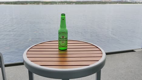 Heineken-Bierflasche-Auf-Dem-Tisch-Auf-Dem-Balkon-In-Einer-Wohnung-In-Der-Nähe-Eines-Ozeanvideohintergrunds-In-4K