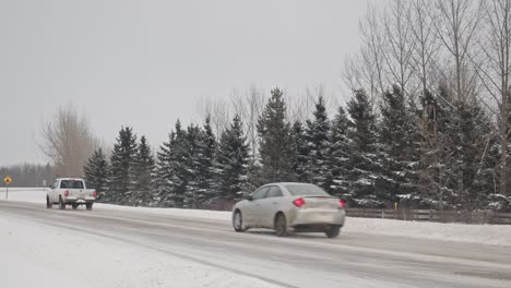 Slomo-of-a-procession-of-passenger-vehicles-driving-on-a-snow-covered-highway-as-it-snows