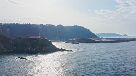 Cudillero-Küste,-Leuchtturm-Und-Hafenseelandschaft,-Sonnenlichtblendung-Auf-Der-Wasseroberfläche,-Luftaufnahme
