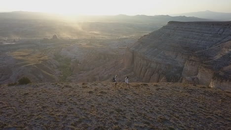 Slo-Mo-sunrise-aerial-of-hikers-on-mesa-above-eroded-fairy-chimneys