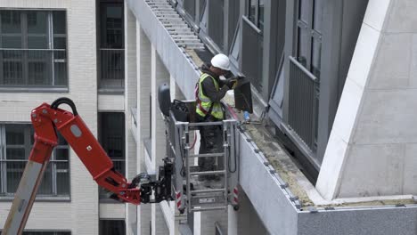 Trabajador-De-La-Construcción-En-Un-Selector-De-Cereza-Usando-Una-Sierra-De-Mano-Para-Cortar-Mosaicos-En-El-Exterior-De-Un-Nuevo-Apartamento-Construido-En-Londres