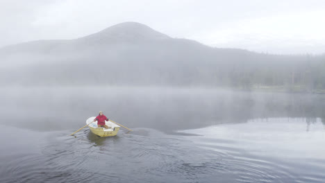 Mann-In-Roter-Jacke-Rudert-Ein-Kleines-Boot-Im-Nebelgefüllten-See