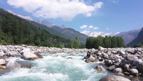 Aerial-shot-of-water-stream-flowing-near-the-rocks-with-a-mountain-in-the-background