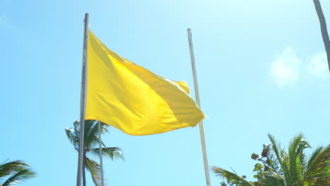 Gelbe-Warnflagge-Am-Mast-Weht-Im-Wind-Am-Strand-Von-Bavaro-Vor-Blauem,-Sonnigem-Himmel