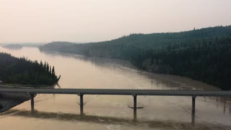 Aerial-drone-forward-moving-shot-over-a-narrow-bridge-along-a-winding-river-along-the-Alaskan-Highway-in-USA-at-dawn