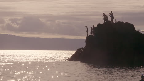Shot-of-man-jumping-off-cliff-into-the-ocean-during-evening-time