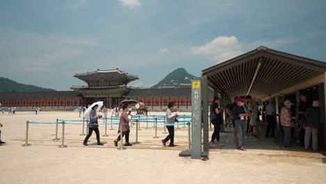 Eine-Menschenmenge-Kommt-Zum-Ticketschalter-Des-Gyeongbokgung-Palastes,-Um-Eintrittskarten-Zu-Kaufen,-Mit-Dem-Heungnyemun-Tor-Und-Dem-Berggipfel-Bukhansan-Im-Hintergrund